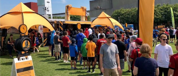 Fans crowding around a branded sports sponsorship activation tent at an outdoor live event on a sunny day