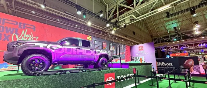 Toyota pickup truck displayed on a turf platform at an interactive Super Bowl fan experience activation, with stanchions guiding fans through the setup.